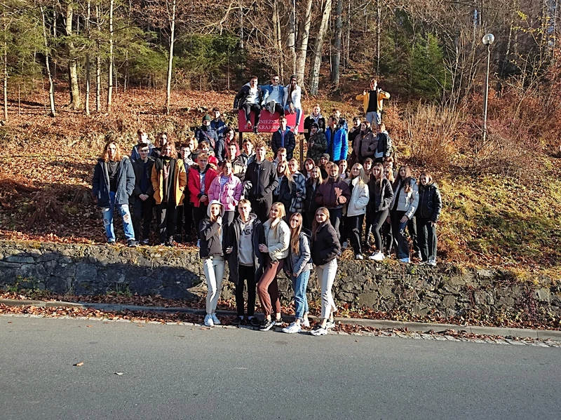 Fotografia przedstawia grupę 49 uczniów z Zespołu Szkoł Nr 1 w Bochni na tle porośniętego lasem wzgórza w scenerii jesiennej. W tle jest widoczny czerwony napis „Śnieżnicki park krajobrazowy”.