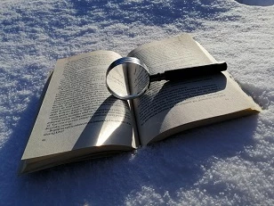 Na zdjęciu widać położoną w śniegu otwartą książkę, a na niej lupę.